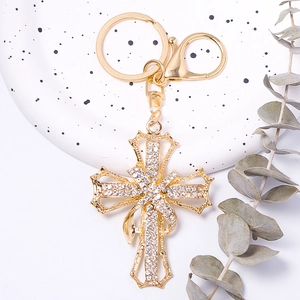 Detail of a gold cross keychain with white rhinestones and a decorative ribbon charm