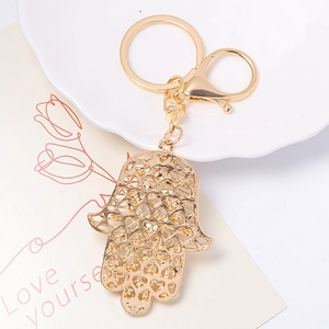 Golden Hamsa hand keychain with hollow heart patterns and lobster clasp on ceramic plate