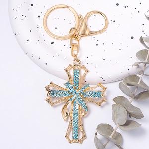 Macro shot of golden cross keychain with light blue rhinestones on white ceramic plate