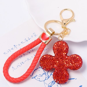 Detail of red sparkling four-leaf clover keychain with gold heart charm and braided cord