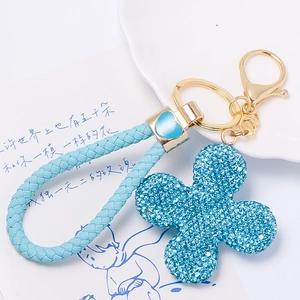 Detail of blue rhinestone clover keychain with gold lobster clasp and braided leather cord