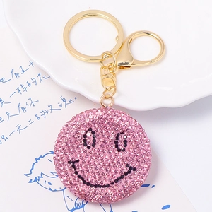 Dettaglio del portachiavi a forma di faccina con strass rosa e chiusura dorata su piatto bianco