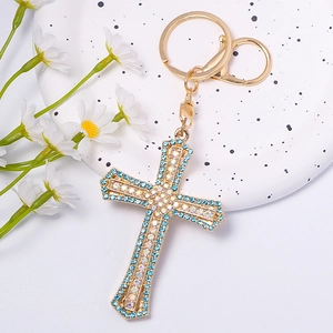 Detailed close-up of golden cross keychain with blue rhinestones on a white ceramic plate