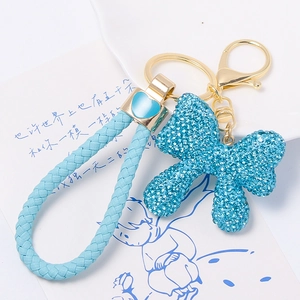 Close-up of blue rhinestone bow keychain with light blue braided leather strap and heart