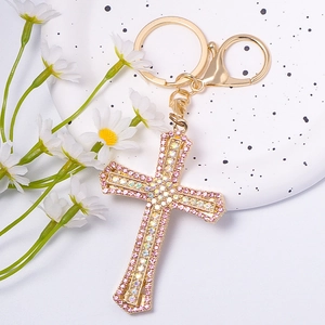 Cross keychain with pink and aurora crystals and golden clasp on a white surface