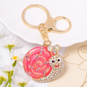 Close-up of golden snail keychain with pink shell and sparkling crystals on white dish