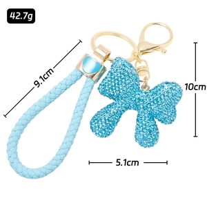 Blue rhinestone bow keychain with braided leather strap and heart charm on white background