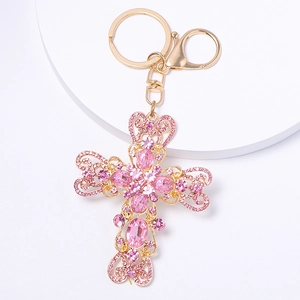Détail du porte-clés croix en or avec strass roses et gravure florale évidée sur blanc