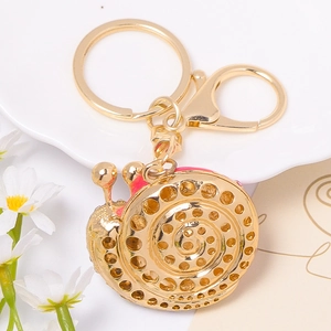 Golden snail keychain with rhinestone details and pink enamel on a decorative tray