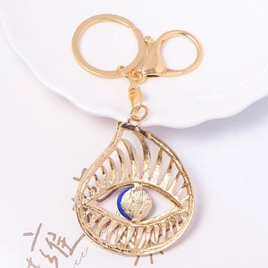 Golden Evil Eye keychain with blue bead on white ceramic tray for bags and car keys
