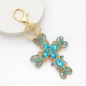 Porte-clés croix doré avec strass bleu ciel et motifs métalliques ajourés sur fond clair