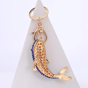 Porte-clés dauphin doré avec strass bleus et fermoir mousqueton sur fond blanc