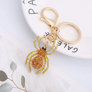 Spider keychain in gold metal with yellow rhinestones on a decorative white porcelain plate