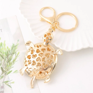 Porte-clés tortue dorée avec motif cœur sur plateau blanc et décor de feuilles vertes