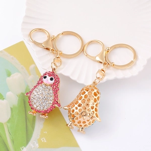 Porte-clés pingouin mignon avec strass roses et dorés sur un plateau blanc élégant