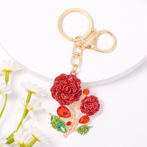 Close-up of golden rose keychain with red crystals and emerald rhinestones on white stand