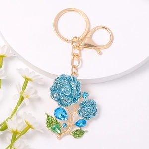 Close-up of gold metal rose keychain with blue and green rhinestones on white display