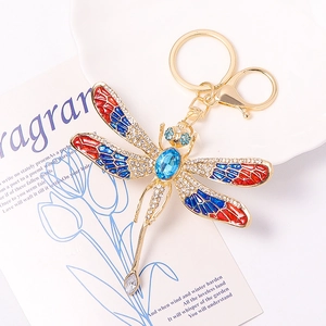 Macro detail of golden dragonfly keychain with colorful enamel wings and blue crystals