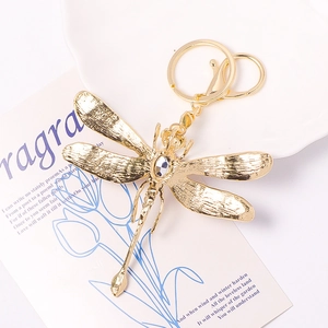 Golden dragonfly keychain with sparkling rhinestone on elegant decorative floral background