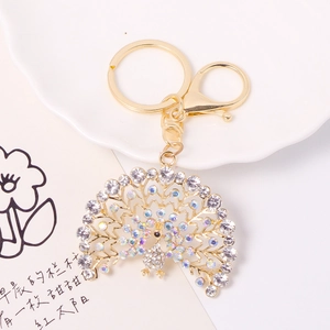 Golden peacock keychain pendant with crystal rhinestones on a decorative ceramic tray