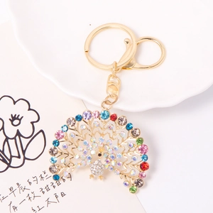 Detailed macro view of gold peacock keychain with colorful rhinestones on a white plate