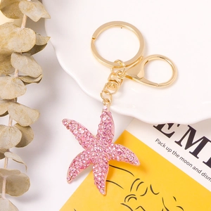 Detail view of a pink rhinestone starfish keychain with gold hardware on a white ceramic plate