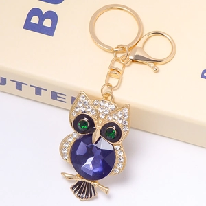 Close-up of golden owl keychain featuring large purple gem and white sparkling rhinestones