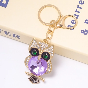 Macro detail of owl keychain featuring a large faceted purple gemstone and green crystal eyes