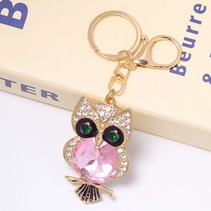 Detailed close-up of a golden owl keychain with pink crystal and green gemstone eyes
