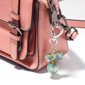 Detail van roze handtas met litchi-nerfleer, vintage gesp en hartvormige kralenhanger
