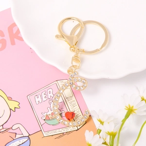 Close-up of gold letter E keychain with white rhinestones and a small red heart charm