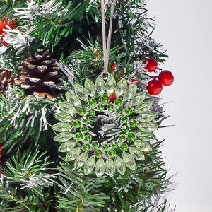 Detail of green crystal starburst ornament on a Christmas tree branch with red berries