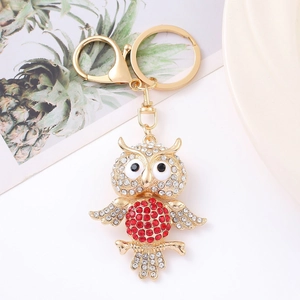 Sparkling owl keychain with gold metal base and vibrant red rhinestones on a white plate