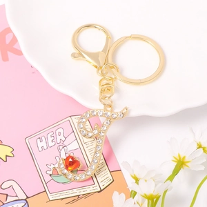 Close-up of golden letter J keychain with white rhinestones and a red heart gemstone