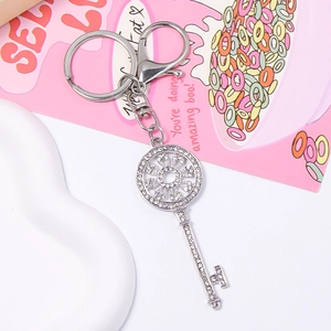 Close-up of a silver key-shaped keychain with rhinestones and floral hollow design