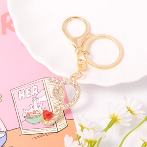 Close-up of gold metal keychain with crystal letter pendant and red heart gemstone