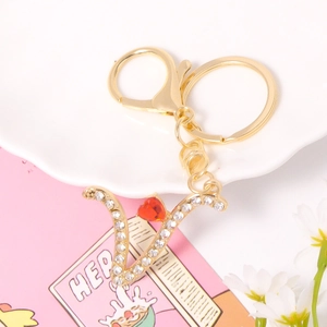 Detailed macro of gold metal V letter keychain with sparkling crystals and a red heart stone