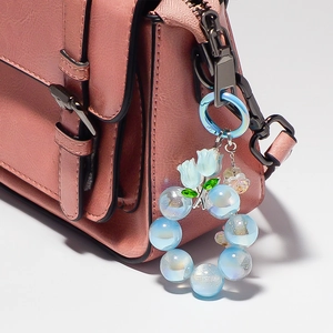 Détail de porte-clés perles tulipe bleue avec finition nacrée sur un sac rose en cuir