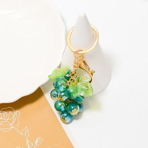 Macro-opname van druif sleutelhanger met blauwe kralen, groene bladeren en gouden sluiting