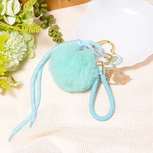 Detail of mint green pompom keychain with braided strap and rhinestone butterfly charm
