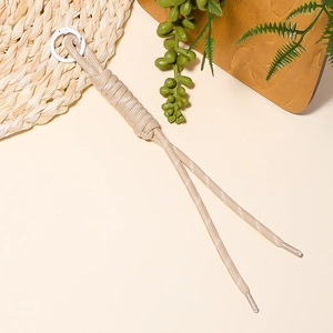 Detailed close-up of champagne braided rope pendant with white ring clip on straw mat