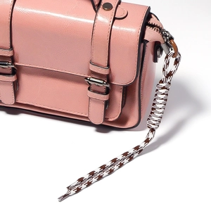 Detail of pink glossy satchel bag with metallic buckles and braided rope ornament