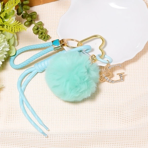 Detail view of gold rhinestone letter G keychain with mint fur ball and woven strap