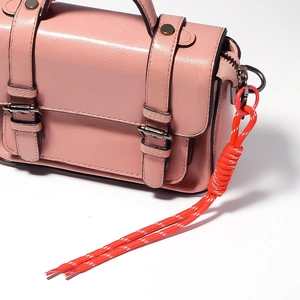 Close-up of a pink PU leather handbag featuring a vibrant red braided rope keychain charm