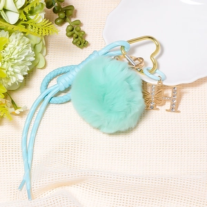 Detail of mint green pompom keychain with heart clip, braided rope and rhinestone H charm