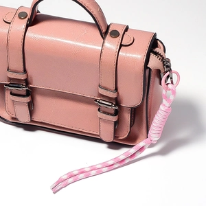 Detail view of a pink messenger bag with metal buckles and a pink braided knot charm