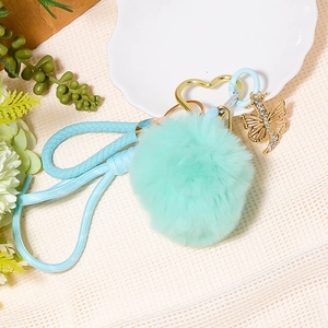 Detail of mint green pom pom keychain with blue woven cord and golden butterfly charm