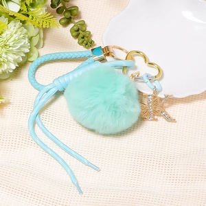 Detail of light blue faux fur pompom keychain with braided leather strap and K letter charm