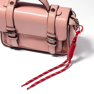 Detail of pink textured crossbody bag with red braided rope pendant and metal buckle trim