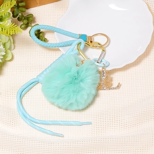 Detailed view of mint green pompom keychain with crystal letter L and blue woven strap
